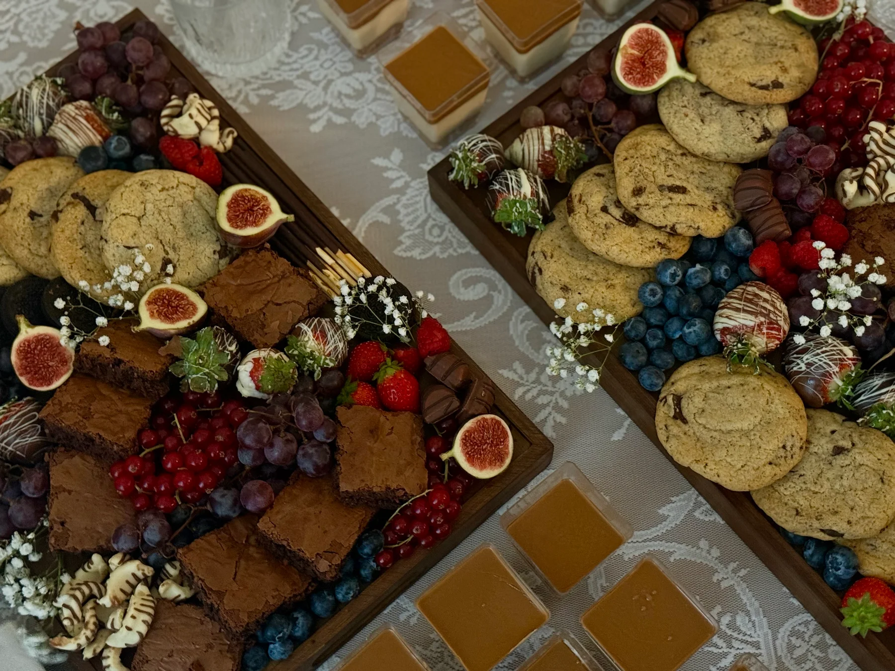 Zwei liebevoll arrangierte Dessertplatten mit hausgemachtem Gebäck, Früchten und Blüten auf einem gedeckten Tisch